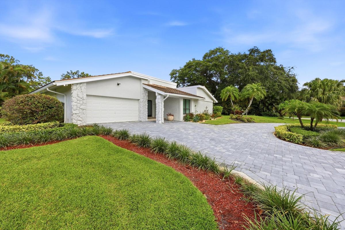 A striking first impression begins with a sweeping paver driveway, lush tropical landscaping, and timeless architectural details that set this home ap