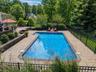 In-ground swimming pool with integrated steps, surrounded by a paver patio and retaining wall, enclosed by black fencing