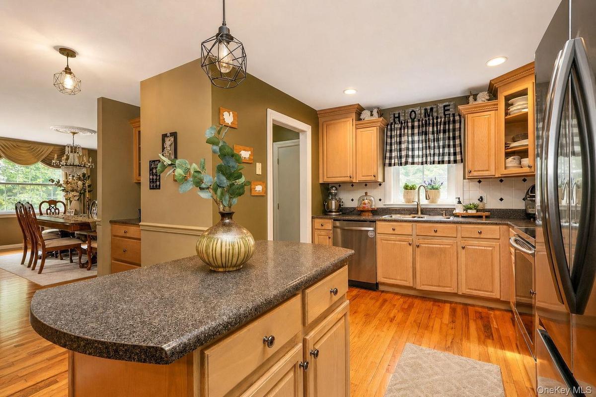 Kitchen featuring wood-finish flooring, light wood cabinetry, dark speckled countertops, center island, stainless steel appliances, and recessed light