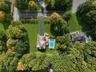 Expansive lot with lush green landscaping, mature trees, a private swimming pool, and a paved driveway leading to the residence