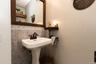 1/2 bath with pedestal sink with dark bronze faucet, tile wainscoting with decorative border, and a wood-framed mirror