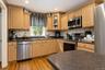 Hardwood flooring, light wood-finish cabinetry, black speckled countertops, recessed lighting, stainless steel appliances, and a tiled backsplash