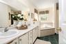 Dual vanity with integrated sinks, a built-in jetted tub, tiled tub surround, separate shower and private toilet room