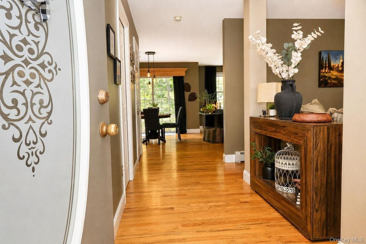 Hardwood flooring extends throughout the hallway, complemented by a decorative entrance door and neutral wall tones