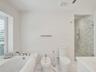 Built-in bathtub with marble surround, glass-enclosed shower with tile surround, bidet, and white wood-finish window shutters