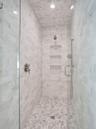 Glass-enclosed shower featuring full-height marble tile work, a recessed ceiling light, and built-in shelving