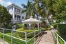 Multi-level building with individual balconies, white gazebo, paved pathway, manicured hedges, and mature palm trees