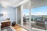 Sliding glass doors opening to a private balcony with glass railings, providing an expansive water backdrop
