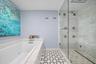 Soaking tub with integrated jets, glass-enclosed shower with multiple body sprays, large format tile shower surround, patterned tile flooring, and int