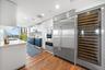 Gourmet kitchen featuring wood-finish flooring, stainless steel appliances, built-in wine refrigeration, white upper cabinetry, and contrasting blue l