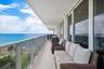 Expansive outdoor balcony with glass and metal railing, offering ocean scenery, a sand beach, and a grassy area