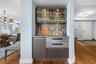 Built-in wet bar with a tiled backsplash, upper illuminated glass cabinetry, integrated under-counter storage, and wood-finish flooring