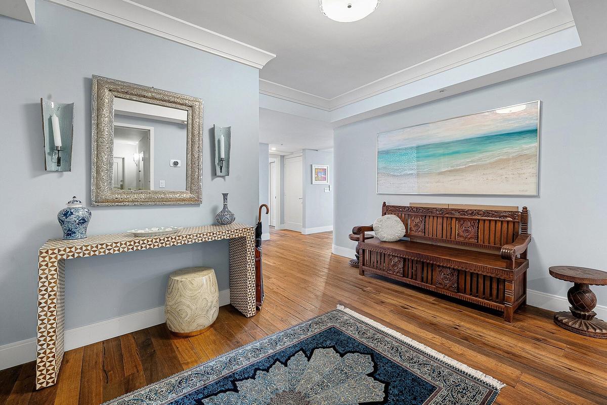 Wood-finish flooring, crown molding, a console table with geometric patterns, and wall sconces