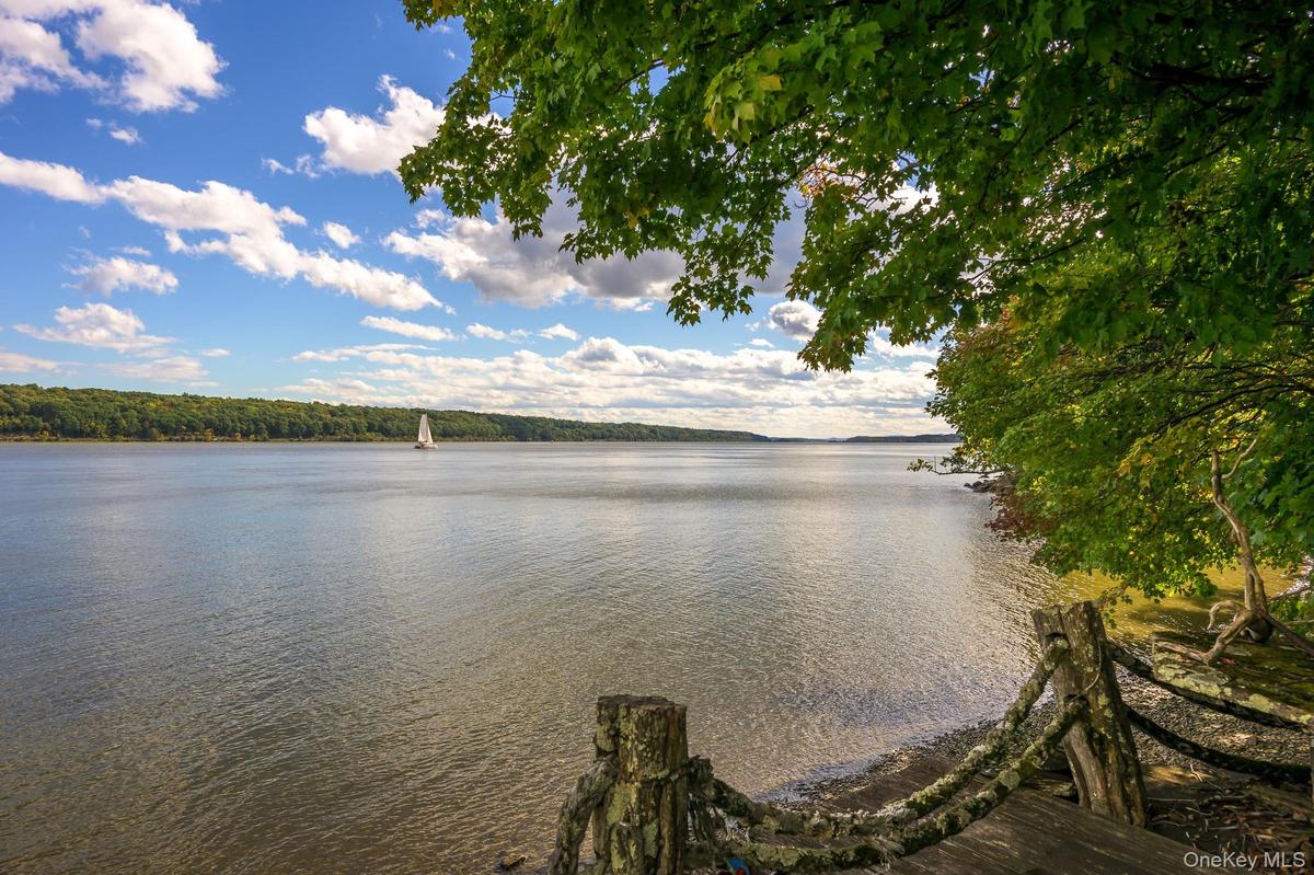 Waterfront property featuring a wood-planked deck, a rustic wood fence, and mature trees framing the natural landscape