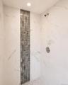 Shower enclosure featuring large format white tile walls with gray veining, a recessed ceiling light, and a vertical mosaic accent strip