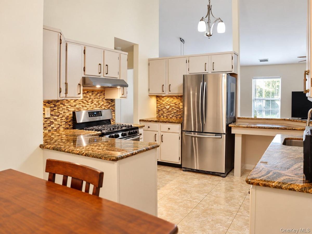 Kitchen featuring vaulted ceilings, light-toned cabinetry, stainless steel appliances, a tile backsplash, and stone countertops