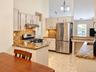 Kitchen featuring vaulted ceilings, light-toned cabinetry, stainless steel appliances, a tile backsplash, and stone countertops