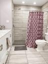 Walk-in shower with wood-look tile surround, tiled flooring, built-in vanity with white cabinetry, and a white countertop