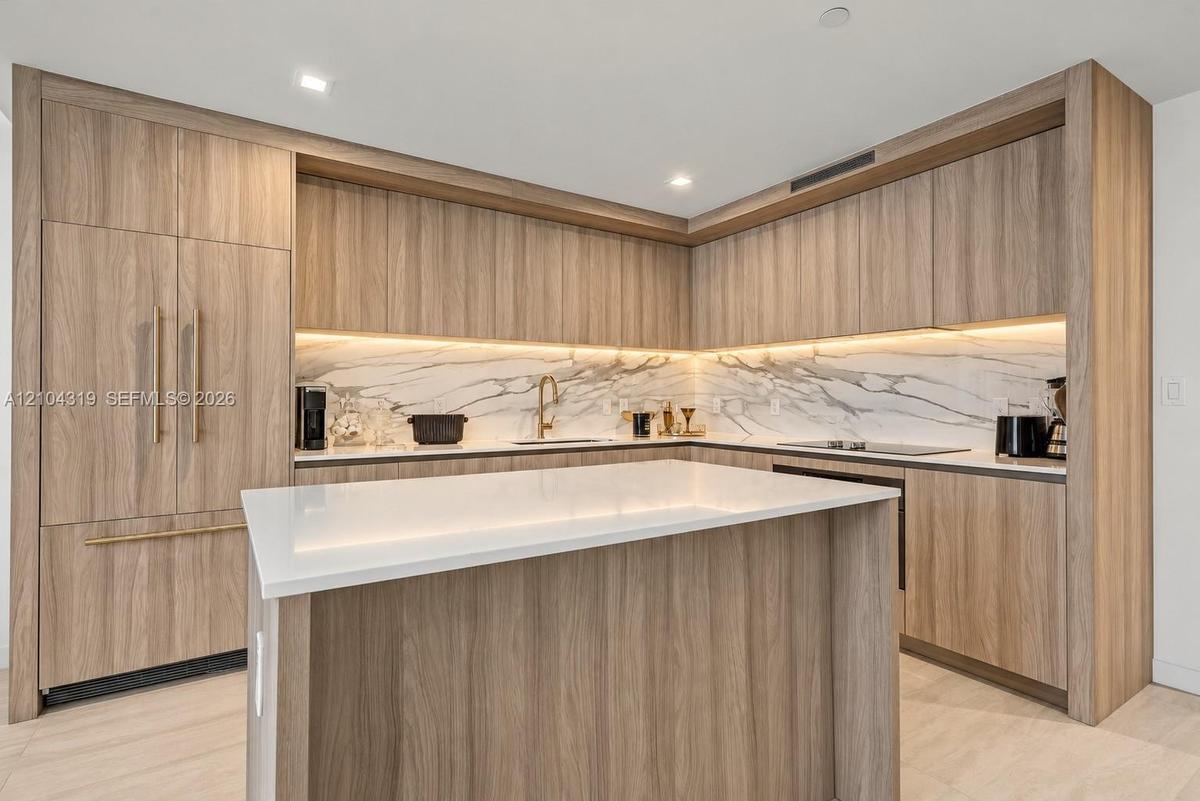 Kitchen featuring wood-finish cabinetry with integrated appliances, stone-patterned backsplash, quartz-topped center island, and recessed ceiling ligh