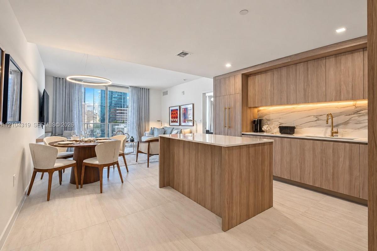 Modern kitchen featuring wood-finish cabinetry, a central island with a stone-surface countertop, integrated appliances, under-cabinet lighting, and s