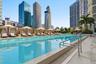 Outdoor swimming pool featuring a tiled edge, metallic handrails, and a surrounding paved deck with shaded cabanas and mature landscaping