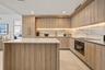 Kitchen featuring custom wood-finish cabinetry, a white stone island countertop, integrated appliances, and a full-height stone backsplash with under-