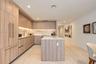 Kitchen featuring wood-finish cabinetry, a waterfall-edge island, stone-patterned backsplash, recessed lighting, and metallic hardware