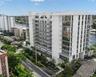 Mid-rise building featuring a white facade, extensive glass paneling, multiple levels of private balconies with railings, and waterfront positioning