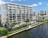 Modern mid-rise building featuring floor-to-ceiling glass windows, wraparound glass-panel balconies, a waterfront bulkhead, and a paved canal-side wal