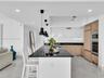 Modern gourmet kitchen featuring an oversized center island with seating, sleek dark stone countertops, stainless steel appliances, and wood-finish ca