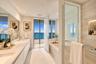 Bathroom featuring a dual-sink vanity with stone countertop, soaking tub, glass-enclosed walk-in shower with tiled surround, and integrated recessed s