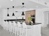 Modern gourmet kitchen featuring an oversized center island with seating, sleek dark stone countertops, stainless steel appliances, and wood-finish ca