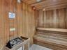 Wood-paneled sauna featuring built-in wood benches, a sauna heater with protective railing, and recessed ceiling lighting