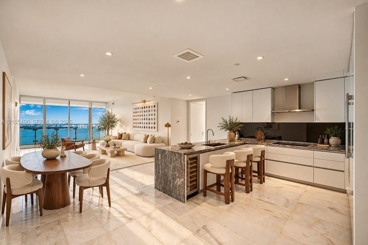 Open-concept living space featuring natural stone flooring, floor-to-ceiling windows, white flat-panel cabinetry, a stone-topped kitchen island with a