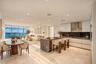 Open-concept living space featuring natural stone flooring, floor-to-ceiling windows, white flat-panel cabinetry, a stone-topped kitchen island with a