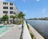 Waterfront pool area featuring expansive stone tile decking, a glass panel railing system, and manicured landscaping