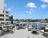 Expansive waterfront balcony featuring large-format stone tile flooring and a glass-paneled railing overlooking the canal