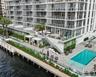 High-rise building exterior featuring tiered balconies with glass railings, a waterfront pool deck, stone-paved sun terrace, integrated pergolas, and 