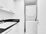 Stacked washer and dryer unit, white cabinetry with silver-tone pulls, black countertop, and an undermount sink with a chrome faucet