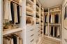 Walk-in closet featuring custom white cabinetry, integrated LED shelf lighting, stacked dresser drawers with metallic pulls, and multiple tiered hangi