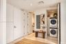 Neutral-toned stone flooring and recessed ceiling lighting throughout, featuring a dedicated laundry closet with a stacked washer and dryer, solid-cor