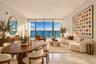 Floor-to-ceiling glass windows, stone flooring, balcony with glass railing, and water backdrop
