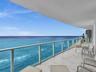 Expansive private balcony featuring glass railings, stone tile flooring, and unobstructed ocean views.