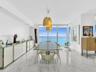 Elegant dining area featuring floor-to-ceiling glass doors and windows, large-format tile flooring, contemporary pendant lighting, and a glass-top din