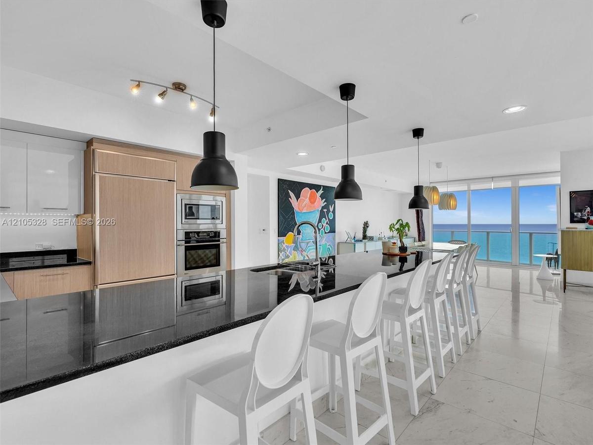 Gourmet kitchen featuring integrated appliances, sleek black countertops, and contemporary pendant lighting.