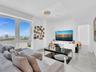 A luxurious and inviting family room, perfect for relaxing or entertaining, featuring expansive windows with captivating city views, elegant white mar