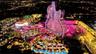Aerial perspective of a multi-structure complex featuring a guitar-shaped high-rise tower, expansive tiered swimming pools, integrated outdoor hardsca