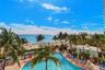Outdoor swimming pool with stone-finish decking, surrounded by mature palm trees, positioned against a backdrop of the coastline and sandy beach