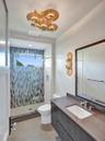 Modern vanity with stone countertop and integrated sink, frameless glass shower enclosure featuring patterned tile surround, and contemporary metallic