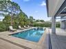 Rectangular swimming pool featuring a tanning ledge, travertine-style tiled deck, and black metal perimeter fencing